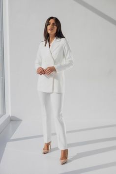 a woman standing in front of a window with her hands on her hips, wearing a white suit and heels