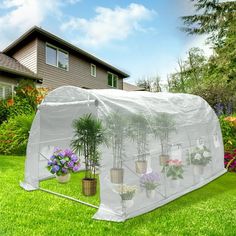 a greenhouse with plants growing in it on the grass near some flowers and trees outside