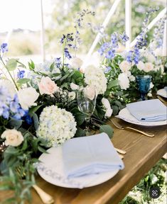 the table is set with blue and white flowers, greenery, and napkins