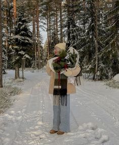 a woman is standing in the snow holding a wreath and looking up at the sky