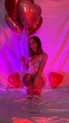 a woman sitting on the floor with balloons in front of her and pink lights behind her