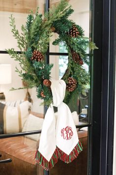 a christmas wreath with pine cones and monogrammed ribbon hangs on the front door