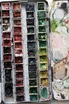 an artist's palette and watercolors in tins on a white surface