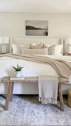 a bed with white linens, pillows and blankets on top of it in a bedroom