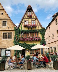 people sitting at tables in front of a building with flowers growing on the side of it