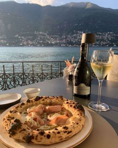 a pizza on a plate next to a bottle of wine and glasses with water in the background