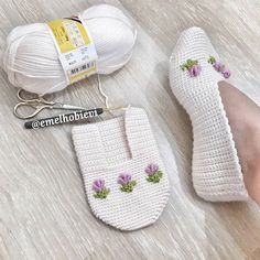 a pair of crochet slippers with flowers on them next to a ball of yarn