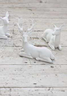 three small white deer figurines sitting on top of a wooden floor next to each other