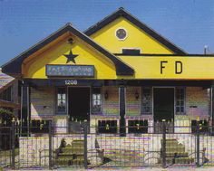 a yellow building with black roof and fenced in area next to it that has green chairs on the outside