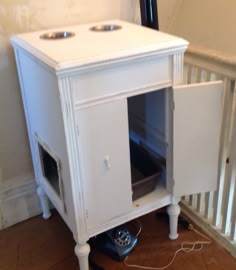 a small white cabinet sitting on top of a floor next to a stair case with an open door