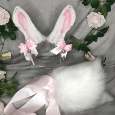 two white bunny ears with pink bows and ribbons on top of a gray blanket next to flowers