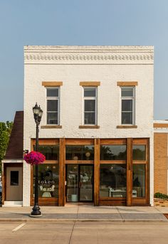 an empty street corner in front of a white building with two windows and a lamp post