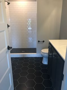 a white toilet sitting next to a shower in a bathroom on top of a black and white floor