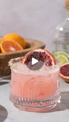 a pink cocktail with blood oranges and limes on the side, sitting in front of other fruit