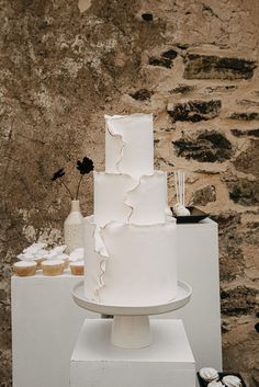 a three tiered white cake sitting on top of a table next to cupcakes