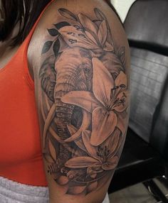 an elephant and flowers tattoo on the arm by a woman in orange shirt with red tank top