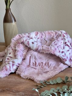 a pink blanket sitting on top of a wooden table next to a vase with flowers