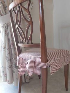 a wooden chair with a striped seat cover on it's back and side, in front of a curtained window