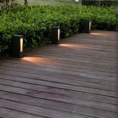 some lights that are on the side of a wooden deck in front of bushes and trees