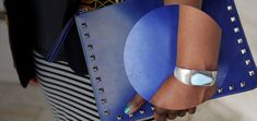 a close up of a person's arm holding a blue purse with an oval design on it