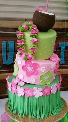 a three tiered cake decorated with pink and green flowers, grass and an umbrella