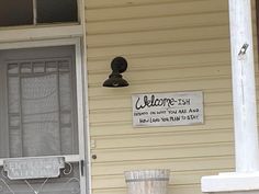 a welcome sign is posted on the front door of a house with a trash can