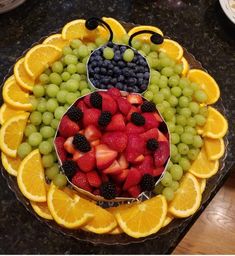 a fruit platter with oranges, grapes, strawberries and lemons in the shape of a lady bug