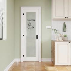 a kitchen with green walls and white cupboards, tile flooring and an open door