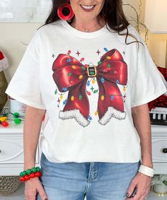 The Red Santa Bow With Lights Graphic Shirt is a festive Christmas design featuring a red Santa bow adorned with twinkling Christmas lights. This cheerful graphic is perfect for the holiday season and is available in short sleeve, long sleeve, and sweatshirt options. Available in sizes YXS to 5XL, this shirt makes a fun, cozy, and stylish choice for Christmas celebrations or lounging during the festive season! Twinkling Christmas Lights, Graphic Shirt, Christmas Design, Festive Season, Festive Christmas, Graphic Shirts, Festival Season, Christmas Lights, The Holiday