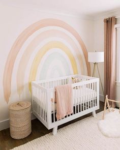 a baby's room with a white crib and large rainbow painted on the wall