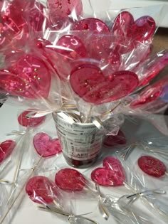 a vase filled with lots of pink hearts on top of a white table next to lollipops