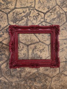 a red frame sitting on top of a stone floor next to a brick wall with cracks in it