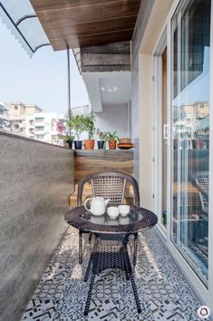 an outdoor table with two cups on it next to a patio area that has potted plants