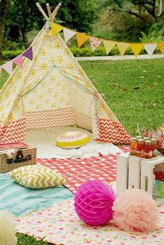 a teepee tent is set up in the grass for a picnic with food and drinks