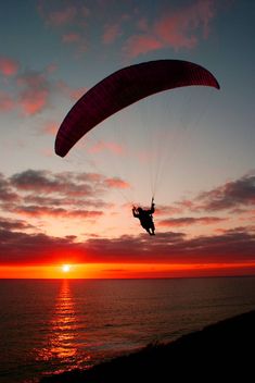 a person is parasailing over the ocean at sunset