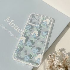 an iphone case sitting on top of a blue box next to some flowers and a plant