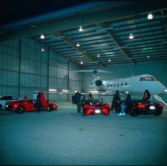 some people are standing around cars in front of an airplane