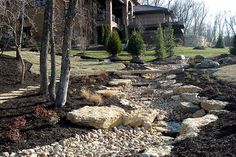 a stone path in front of a house with trees and rocks on the ground next to it