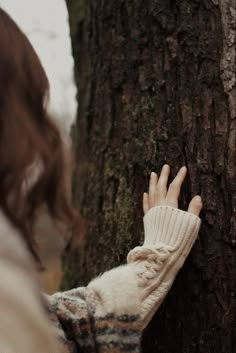 a woman touching the trunk of a tree with her hand on it's side