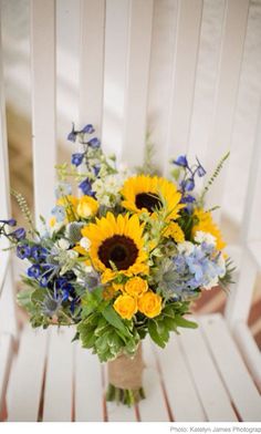 a bouquet of sunflowers and blue flowers on a white chair with wood slats