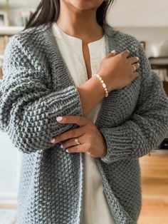 a woman standing in a room wearing a gray cardigan sweater and pearl bracelets