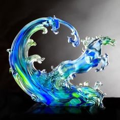 a glass sculpture of a horse on top of a wave in blue and green colors