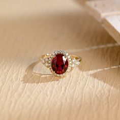 a ring with a large red stone surrounded by small white diamonds on a wooden surface