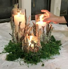 someone is lighting candles in the center of a table with moss and branches on it