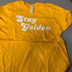 Stay Golden Tshirt Size Youth Xl Sporty T-shirt For Spring Fan Merchandise, Tan T-shirt For Spring Streetwear, Gold T-shirt With Letter Print For Summer, Trendy Gold T-shirt For Summer, Trendy Gold Summer T-shirt, Relaxed Fit Tan T-shirt With Text Print, Tan Graphic Tee With Letter Print, Gold Tops With Logo Print For Streetwear, Casual Gold T-shirt With Logo Print