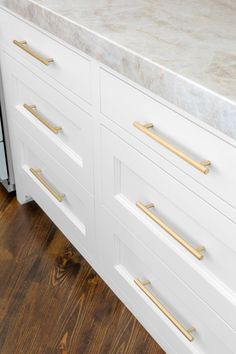 a kitchen counter with white cabinets and gold pulls on it's doors, in front of a wood floor