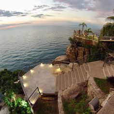 stairs lead up to the top of a cliff by the ocean at dusk with people standing on it