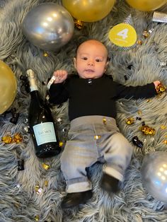 a baby is laying on the floor next to balloons and champagne bottles with confetti around it