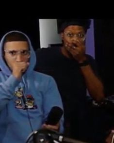 two men are sitting in front of microphones and one is wearing a blue hoodie