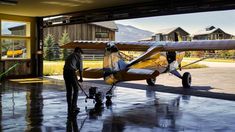 a man standing next to an airplane in a hangar with another person looking on from the other side